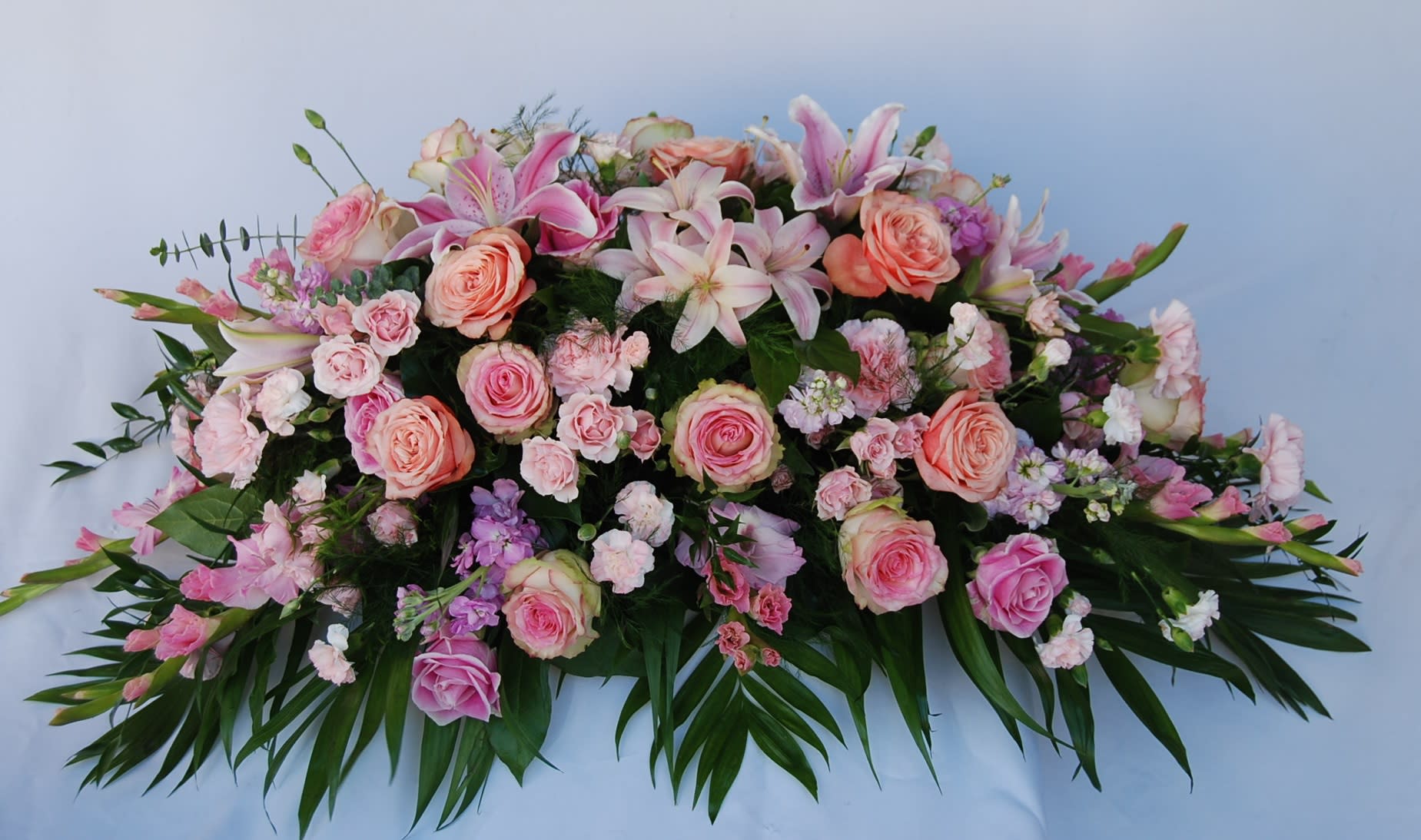 Pink Tribute Casket Spray - A pastel casket arrangement made of pink gladiolus, lilies, roses, spray roses, stocks, and carnations.
