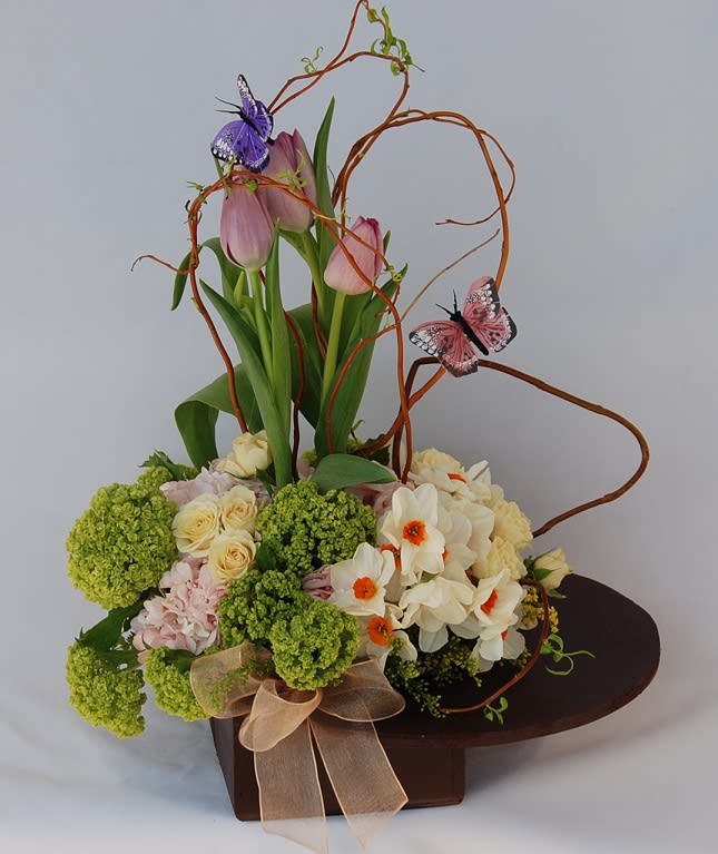 Spring Blooms -  Happy and delightful arrangement of tulips, spray roses, green viburnum, fragrant narcissus, and pink hydrangeas. We emphasized the arrangement with curly willow and charming butterflies in a unique wooden container. 