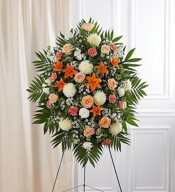 Peach, Orange &amp; White Sympathy Standing Spray - They drew people in with their welcoming smile and personality. That joyful spirit is captured in our classic standing spray arrangement. Crafted with warm orange, peach and white blooms, this elegant display creates a touching tribute to someone who brought happiness to so many.