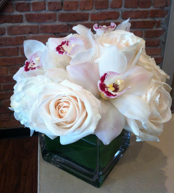 White roses and orchids arranged in a square glass vase