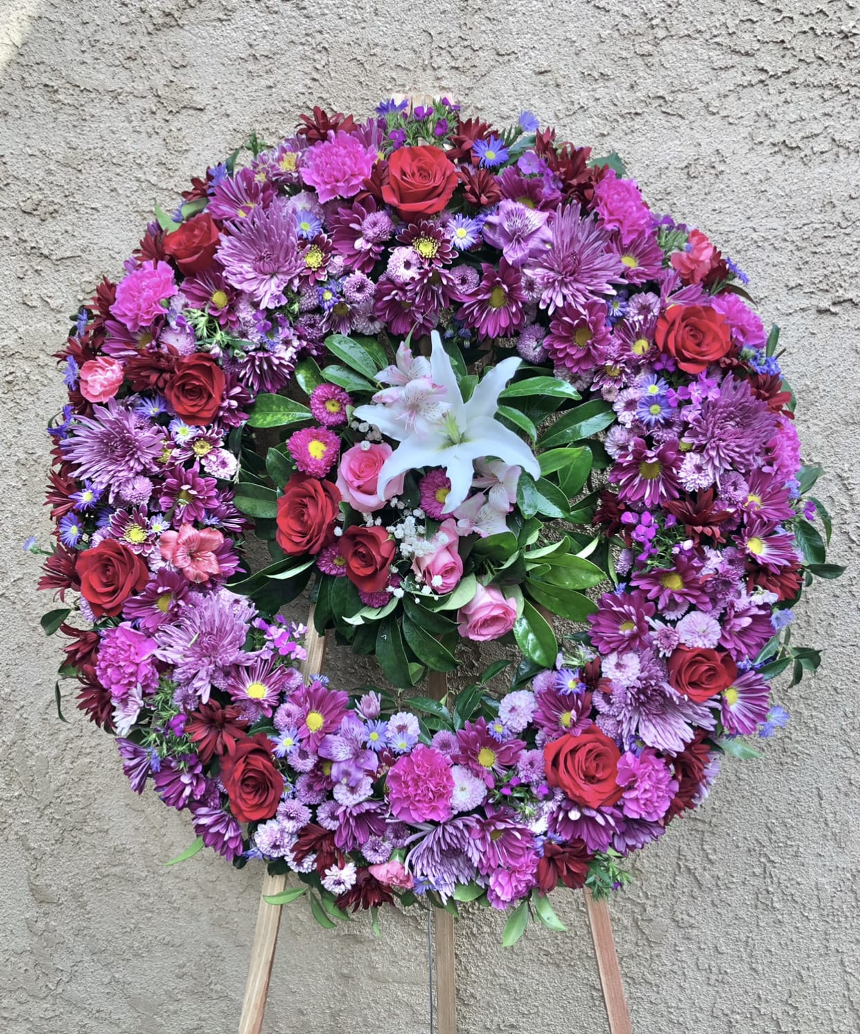 A Spring Mix - Beautiful funeral spray arrangement featuring purple chrysanthemums, daises, red roses, white lilies, pink carnations and green accents