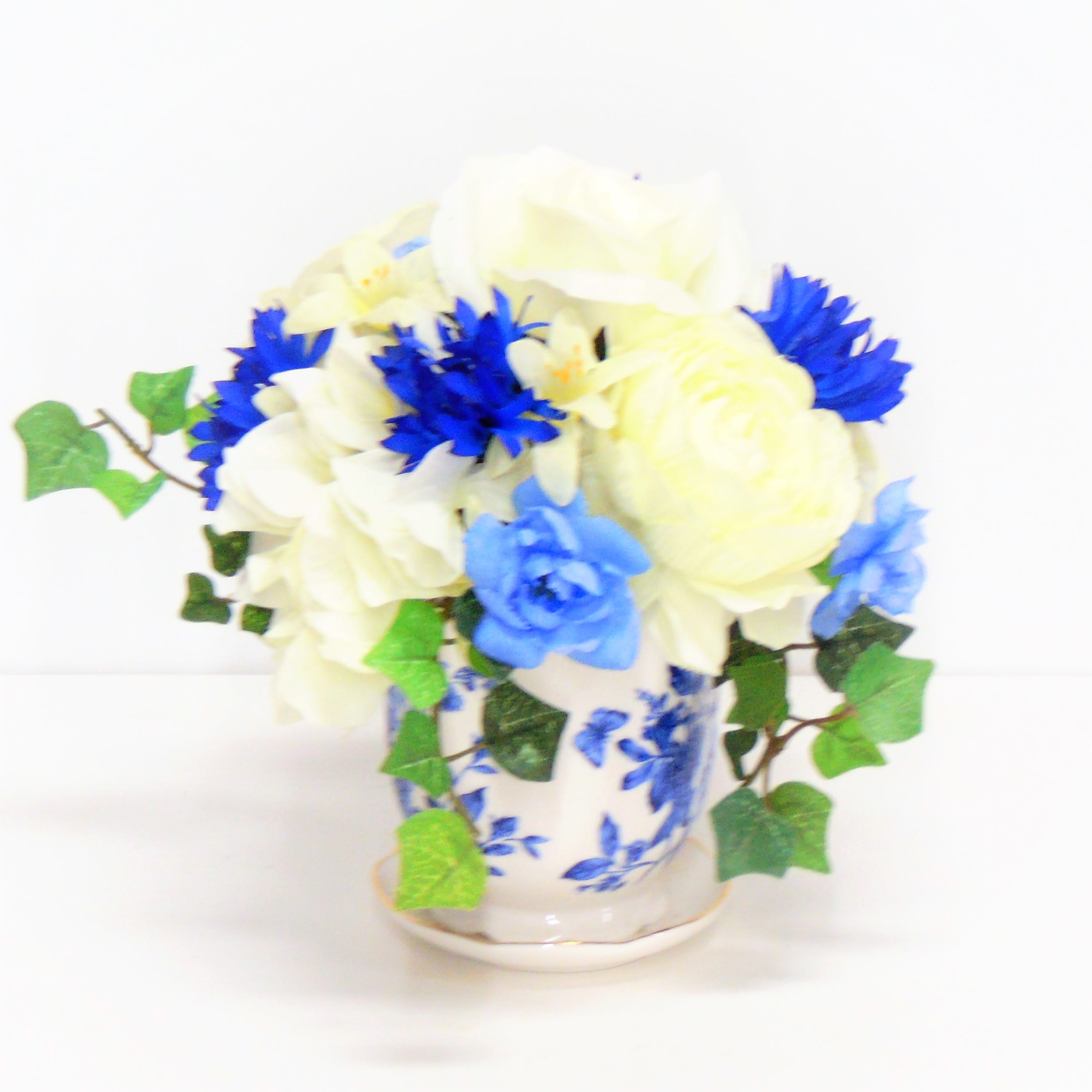 Blue Button Mini Silk Pot - A delicate blue floral pot filled with creme roses, blue bachelor buttons and accents of ivy.. 