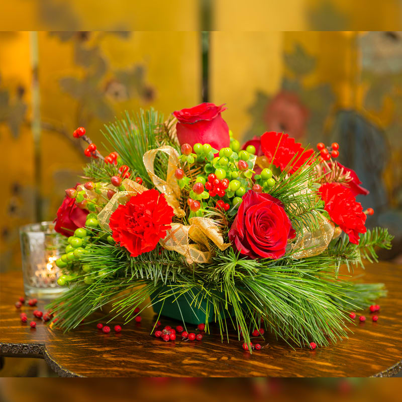 ROSE- CARN DELIGHT - A CENTERPIECE FOR A MORE INTIAMATE SETTING. THIS BEAUTIFUL DESIGN HOLD ROSES, CARNATIONS AND A MIX OF CHRISTMAS BERRIES AND GREENS. POPS OF GOLD RIBBON WILL LOOK RADIANT AGAINST YOUR CHRISTMAS DECOR!
