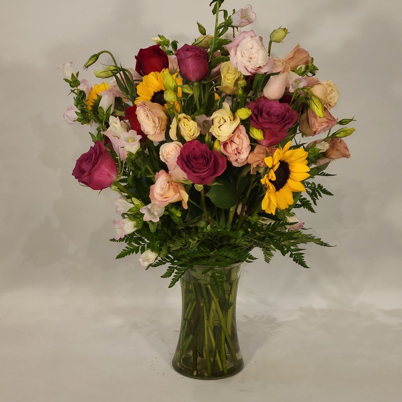 The Megan - Red Roses, Sunflowers, Pink Capanula, Pink Lisianthus, Light Pink Roses and greenery in a tall gathering vase will be perfect for multiple occasions. The other office ladies will be so jealous!