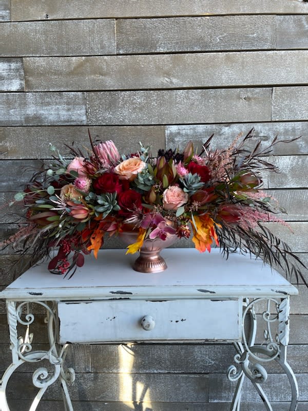 Autumn's Blessings - Gorgeous and lavishly exquisite luxury floral arrangement of ONLY the finest Autumn elements. Perfect for ANY dinner table this is a classy long and low arrangement in a very nice metal pedestal container in rose gold with burgundy and peach accents with dusted succulents. Stunning win win every time you order this one of a kind piece.