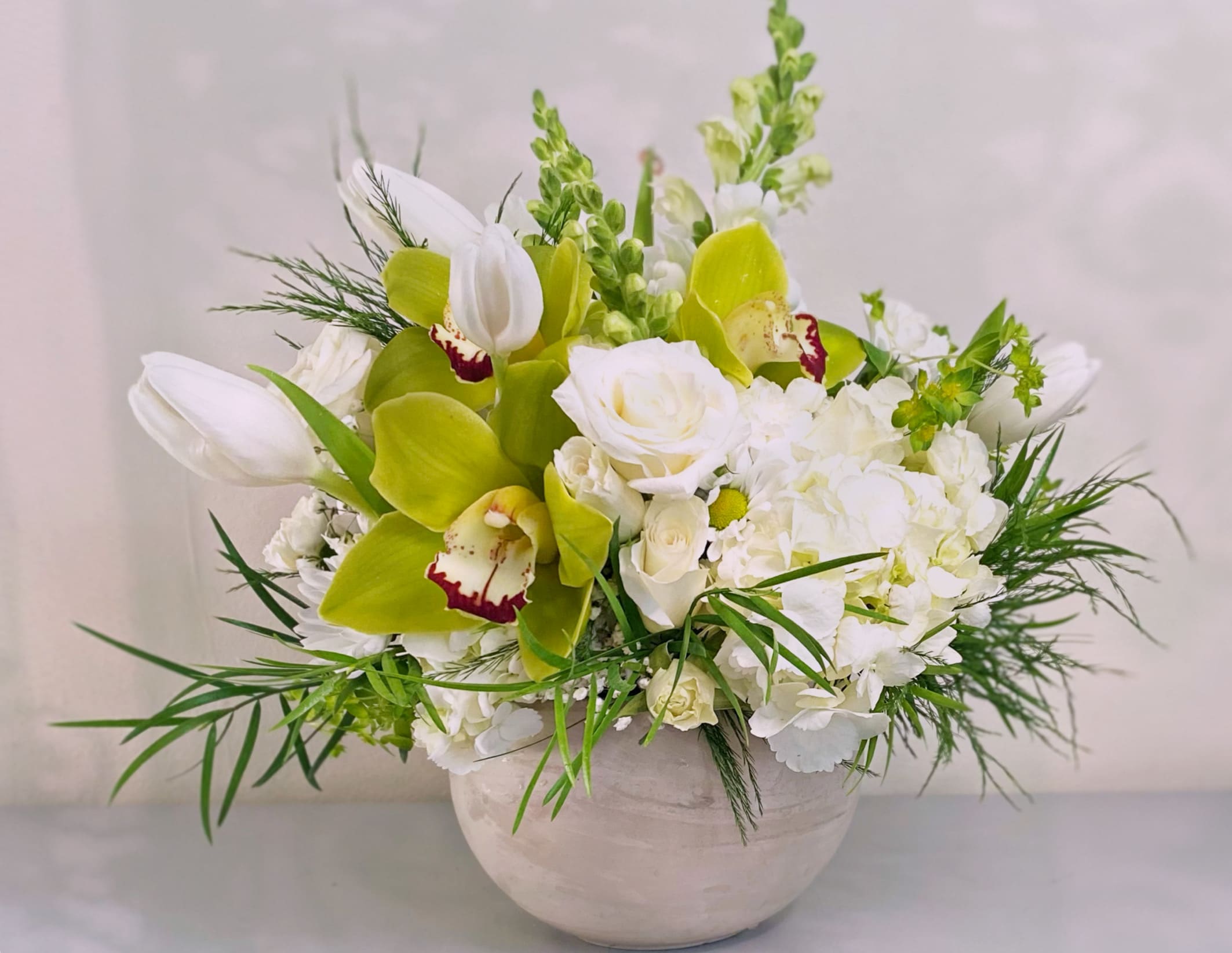 The bright White Bowl - Moving into winter and the holidays with this all white and green floral design. Mixed garden and winter foilages, and all premium white flowers and hints of green hues, finished off with succulents. Approximately 12x10 in size. Comes in a 6 in light tan ceramic bowl. We pick the freshest Premium flowers from the market and we will use substitutions. For instance if the gerbers are not perfect we will opt to use white cymbidium or other similar blooms. 