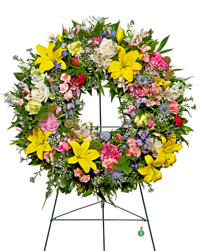 Warm Thoughts Wreath - *Please be aware that florals shown may be substituted based on availability and season.* A bright standing wreath of greenery and fresh flowers in yellow, pink, blue and white will send a message of hope and harmony, and help to celebrate a meaningful life.