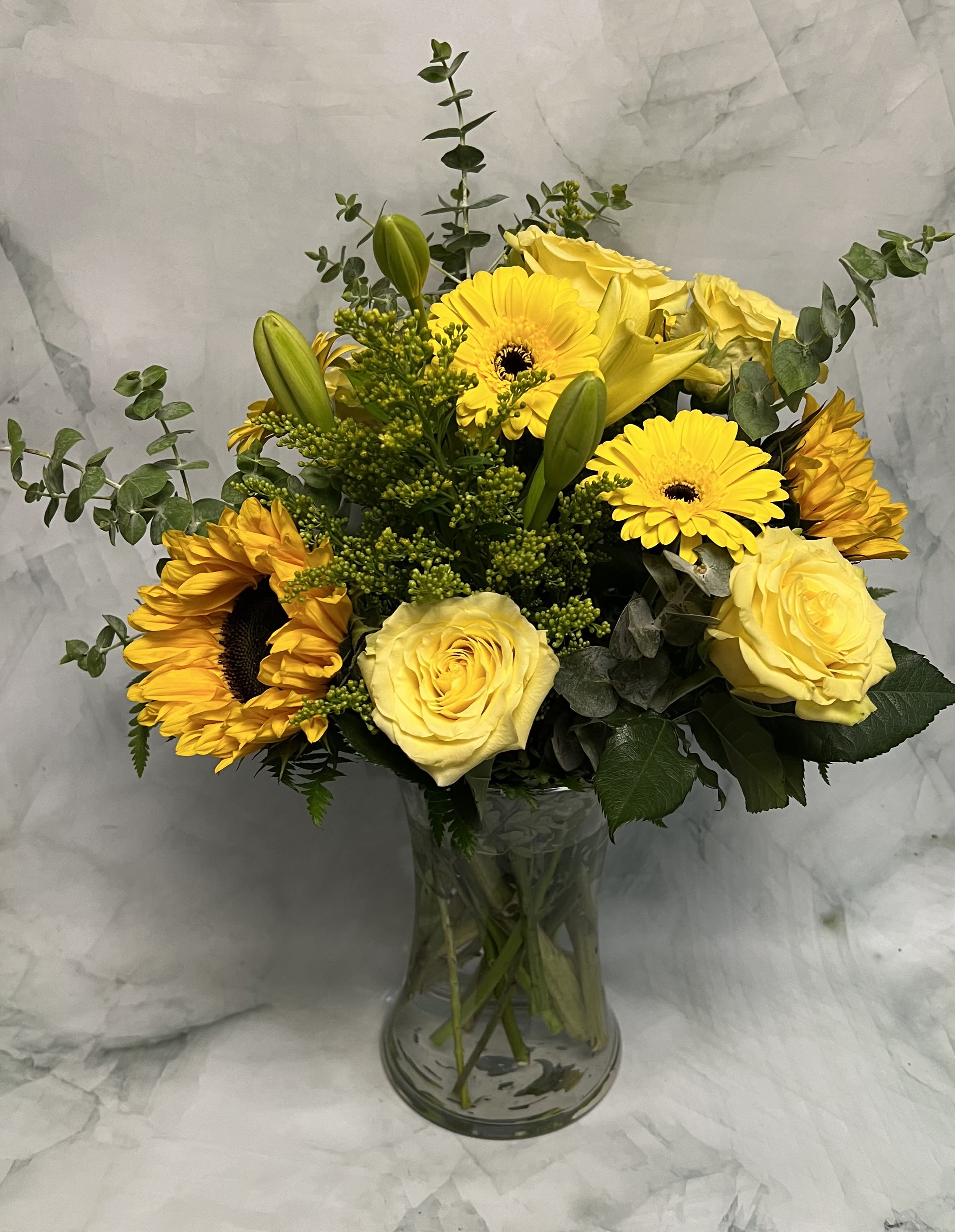 Lovely Sunshine - This arrangement is a ray of sunshine on a cloudy day. Cheer someone up with this bold arrangement filled with yellow flowers. This includes Sunflowers, Eucalyptus, Aster, Roses, and Gerber Daisies. 