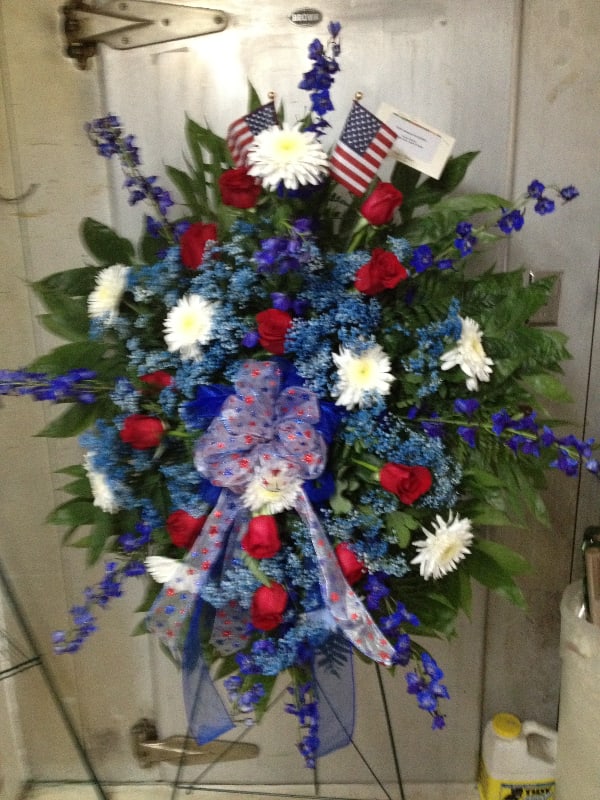 Patriotic Sentiment - * Red roses * Blue delphinium * Gyp * White cremones * 2 American flags * Red white and blue bow * 48&quot; Stand God bless America and those who served. This standing spray is an excellent way to show sympathy for veterans and those left behind.