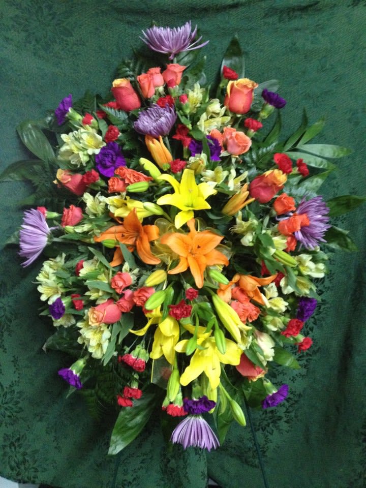 Rainbows End - Colorful standing spray. Orange and yellow lilies, lavender spider mums, purple carnations, roses, red mini carnations, spray roses and alstroemeria make up this bright spray. This is the perfect floral tribute for a loved one. 