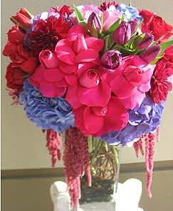 Berry Lush - This romantic arrangement is composed of red, purple and fuscia blooms. It is designed in a tall pyramid vase with rocks and curly willow inside. It has purple hydrangeas, red and purple tulips, red, fuscia and lavender roses, dahlias and red amaranthus hanging down the vase.