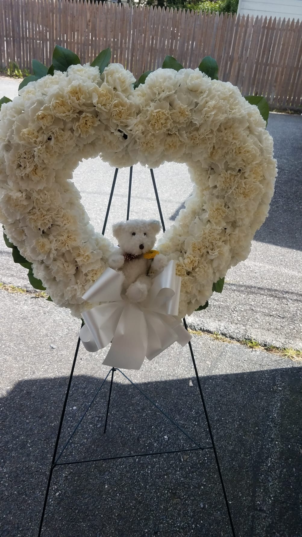Youthful Farewell - A heart covered in white carnations featuring a small teddy bear in the center of your heart