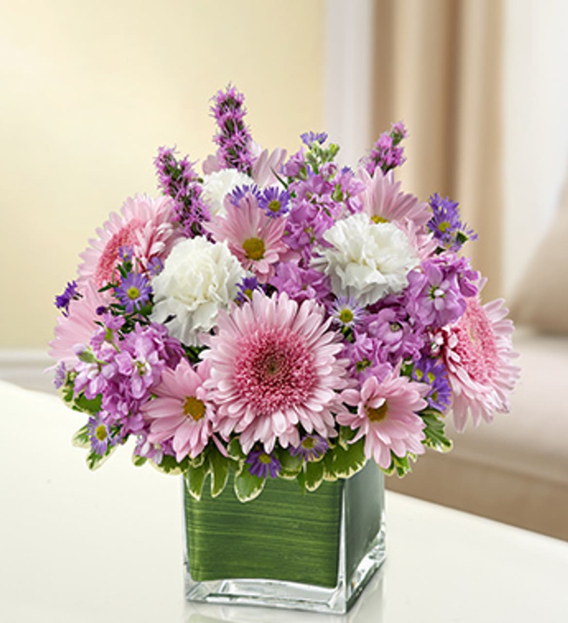 Luscious Lavender  - Let the comforting beauty of elegant lavender and white blooms send a caring message of your sympathies. Lovely roses, stock, liatris, cremones, carnations and more are gathered by hand in a classic cube vase and sent to the home or service to honor lost loved ones. Elegant lavender and white arrangement of roses, stock, liatris, cremones, carnations, daisy poms and monte casino, accented with variegated pittosporum Artistically designed by our florists in a classic clear glass cube vase lined with a Ti leaf ribbon; vase measures 5&quot;H x 5&quot;D Appropriate for the service or for sending to the home or office of friends and family members Large arrangement measures approximately 11&quot;H x 11&quot;L Medium arrangement measures approximately 10&quot;H x 10&quot;L Small arrangement does not include roses and measures approximately 9&quot;H x 9&quot;L Our florists hand-design each arrangement, so colors, varieties, and container may vary due to local availability Please note container &amp; fillers may vary.