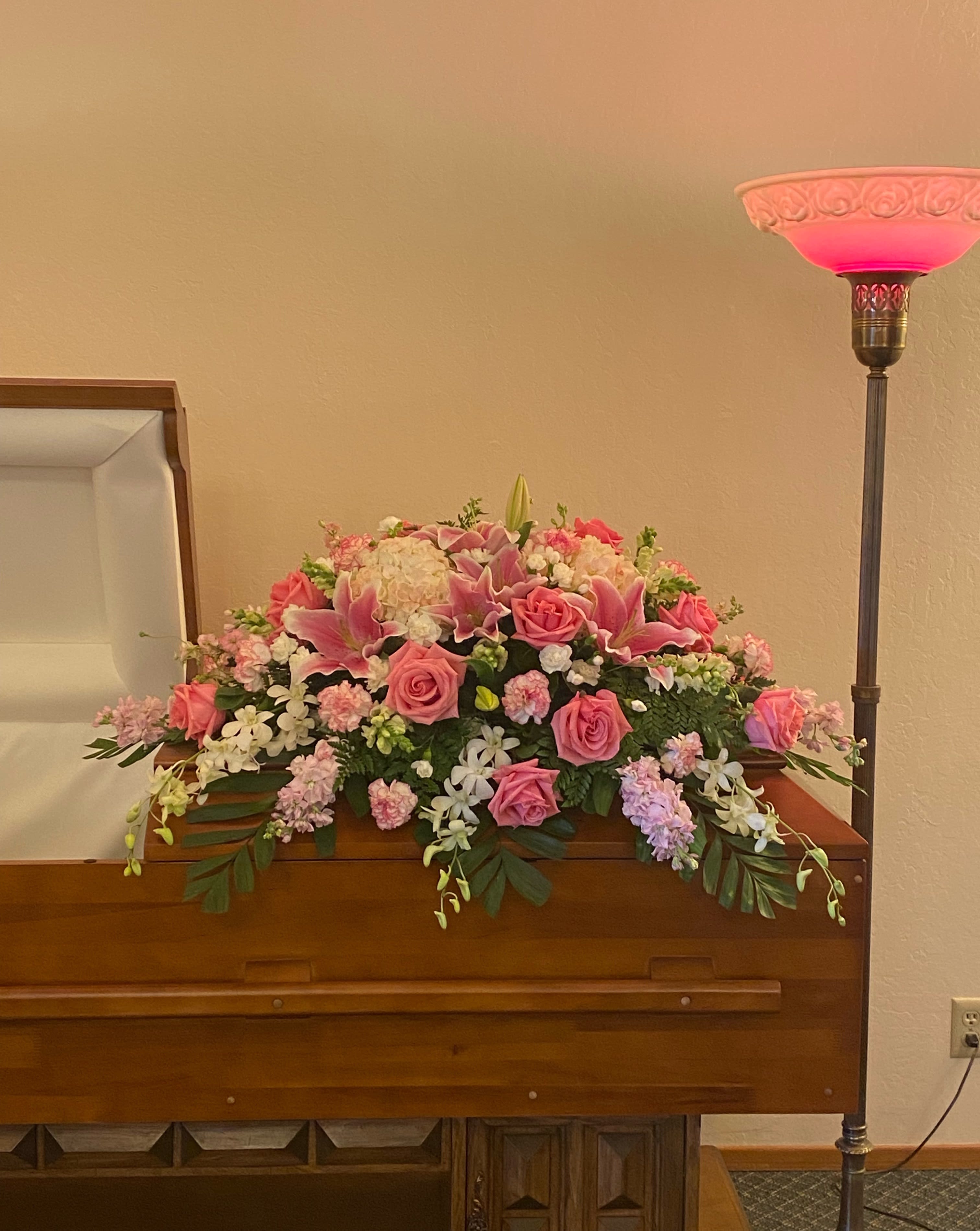 CS#06 Pink &amp; White Casket Spray - A pink and white casket spray featuring lilies, roses, hydrangeas, carnations, snapdragons, and filling greens.  The standard (half-open casket) arrangement is approximately 38” W x 16” H. (As shown) The deluxe (closed casket) arrangement is approximately 46” W x 16” H
