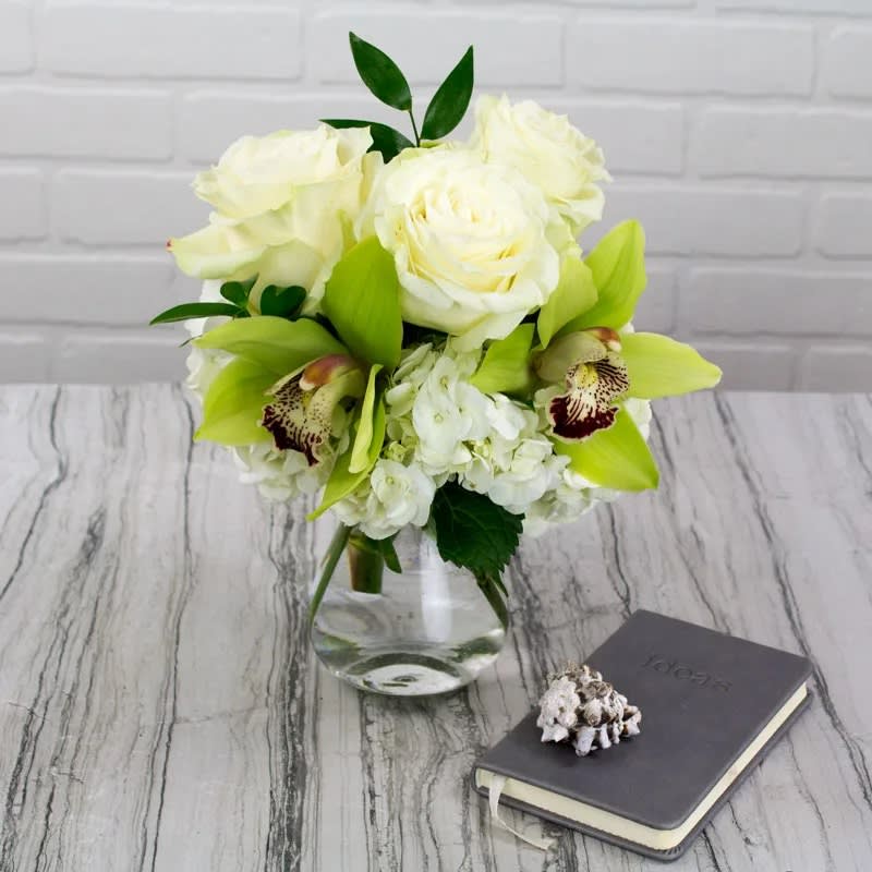 Dainty Duet - David Z Designs - Sometimes something small and sweet is all you need to say a million words for a million reasons. We love this little duo showing off a petite selection of White Roses and Pistachio Green Cymbidium Orchids in a clear glass vase. Perfect for a desk or tableside. 