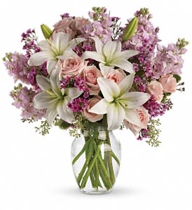 Teleflora's Blossoming Romance - by Collene's Crafts-N-Flowers - Love is in the air. Or if it isn't it will be when you surprise her with a gorgeous array of light pink spray roses fragrant white lilies and other favorites in a sparkling glass vase. You know when she'll love it the most? When it's a total surprise. This lovely bouquet includes light pink spray roses white asiatic lilies lavender stock and lavender waxflower accented with assorted greenery. Delivered in a glass rose vase.Approximately 17&quot; W x 17&quot; H Orientation: All-Around As Shown : TEV09-1ADeluxe : TEV09-1BPremium : TEV09-1C