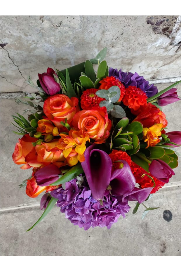 Awaking Awaking - An organic explosion of colors mix with hydrangea, purple callas, tulips and vibrant orange roses, with a light accent of organic greens in a clear vase.