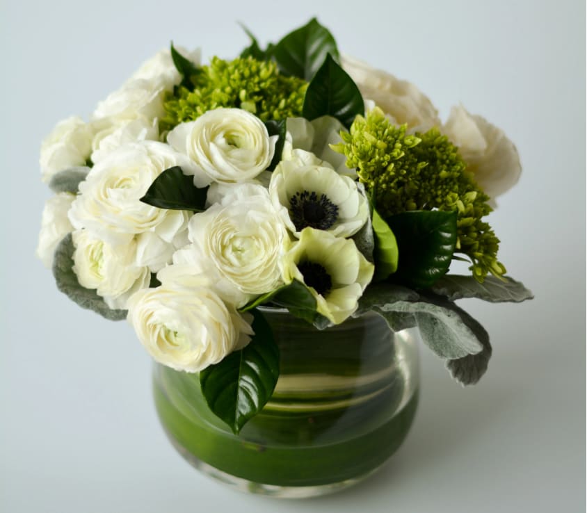 Ivory Ivory - an elegant flower arrangement of white ranunculus and beautiful white anemones with a touch of two-toned greenery presented in a clear vase with a leaf around