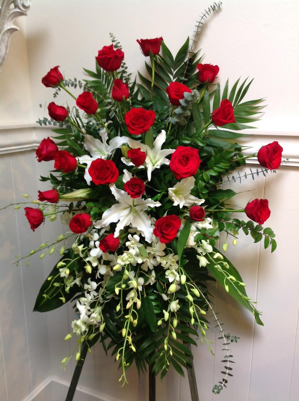 Sweet Serenity - This beautiful easel spray is full of red roses, lilies and orchids. With soft greens, this will make a beautiful addition to any memorial or celebration of life.