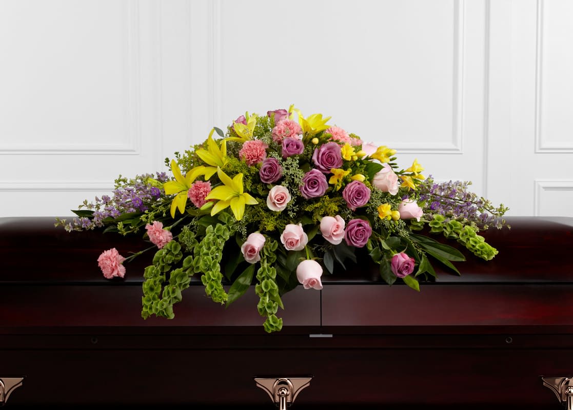 Forever Beloved Casket Spray - Casket Spray beautifully illuminates the atmosphere of their final farewell service. Lavender roses, pink roses, lavender larkspur, pink carnations, Bells of Ireland, yellow Asiatic lilies, yellow freesia, solidago and lush greens are arranged to create an extravagant display of floral beauty that offers comfort and peace to the friends and family of the deceased.