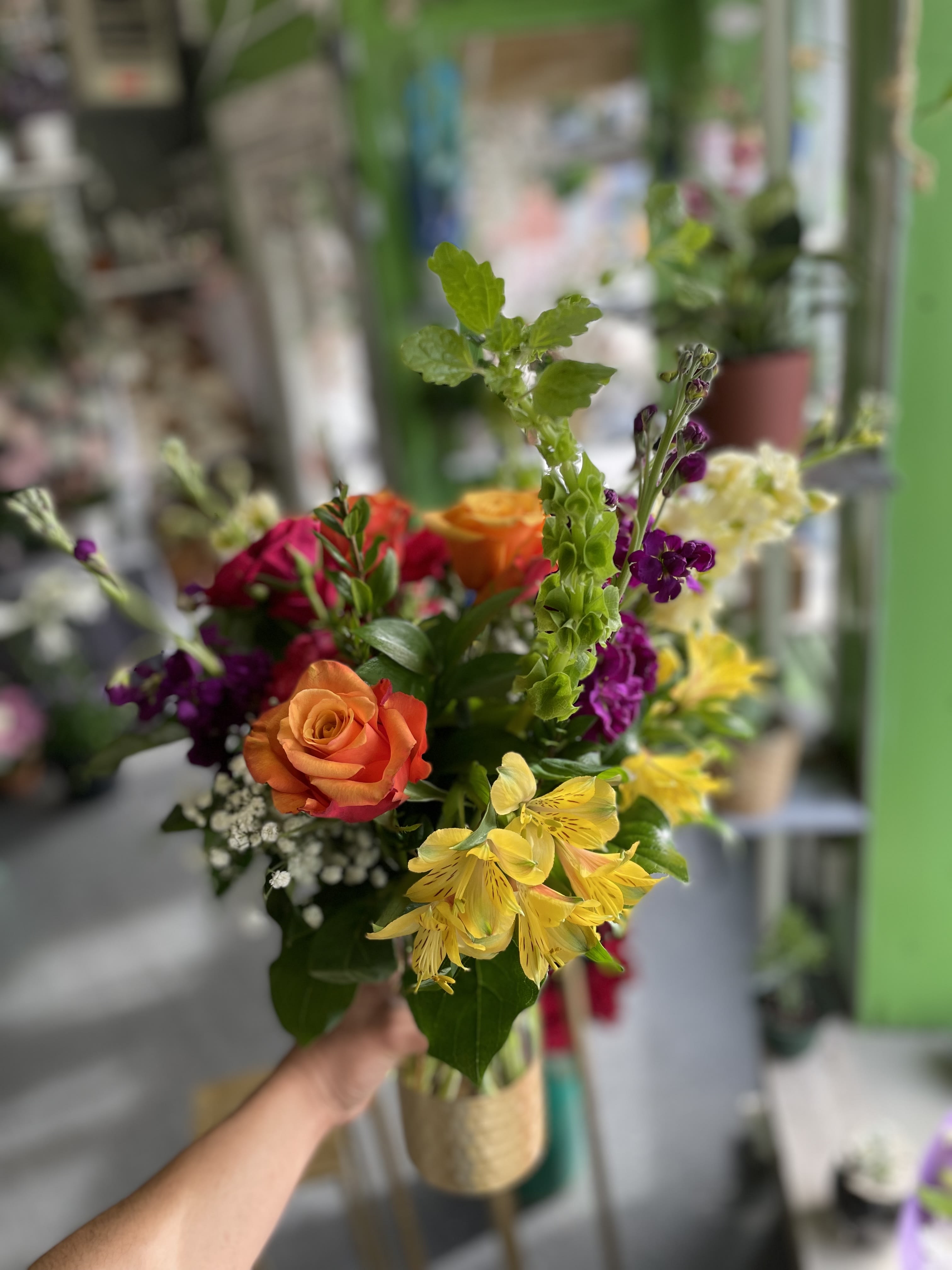 A New Day - This beautiful arrangement has gorgeous colors and has yellow alstro, orange roses, hot pink spray roses, yellow stock, purple stock, green bells of Ireland, hot pink carnations, and fresh-cut greens.