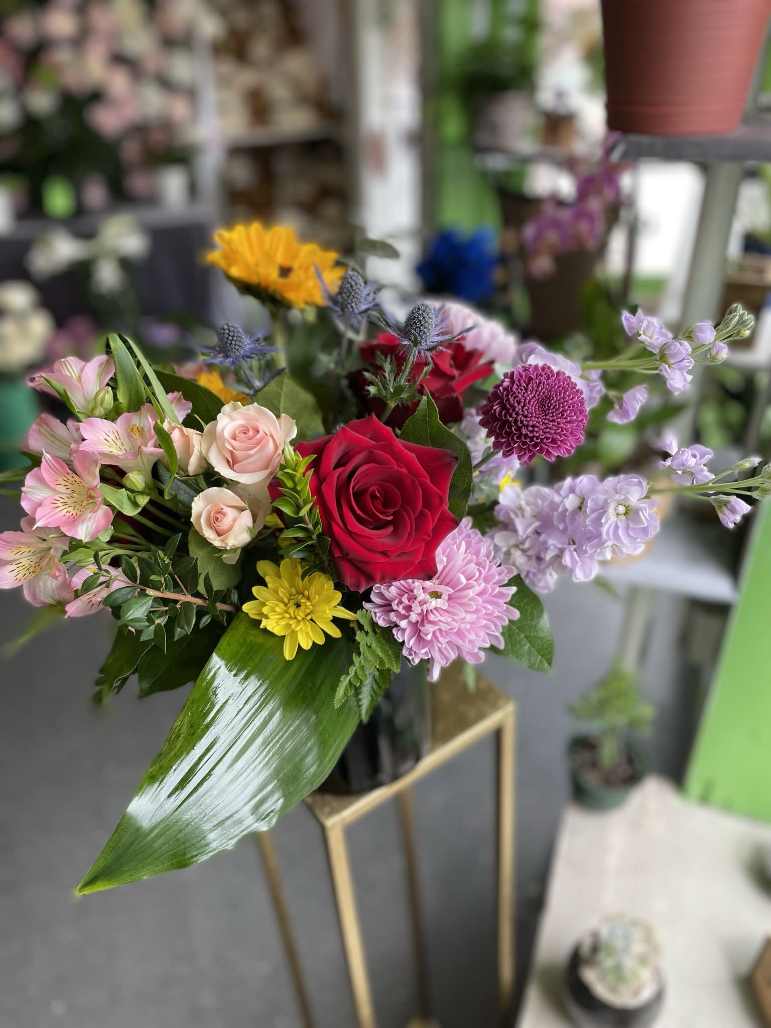 Forever Love  - This gorgeous arrangement has red roses, sunflowers, pink spray roses, lavender mums, pink altros, lavender stock, yellow pom poms, and fresh greens.
