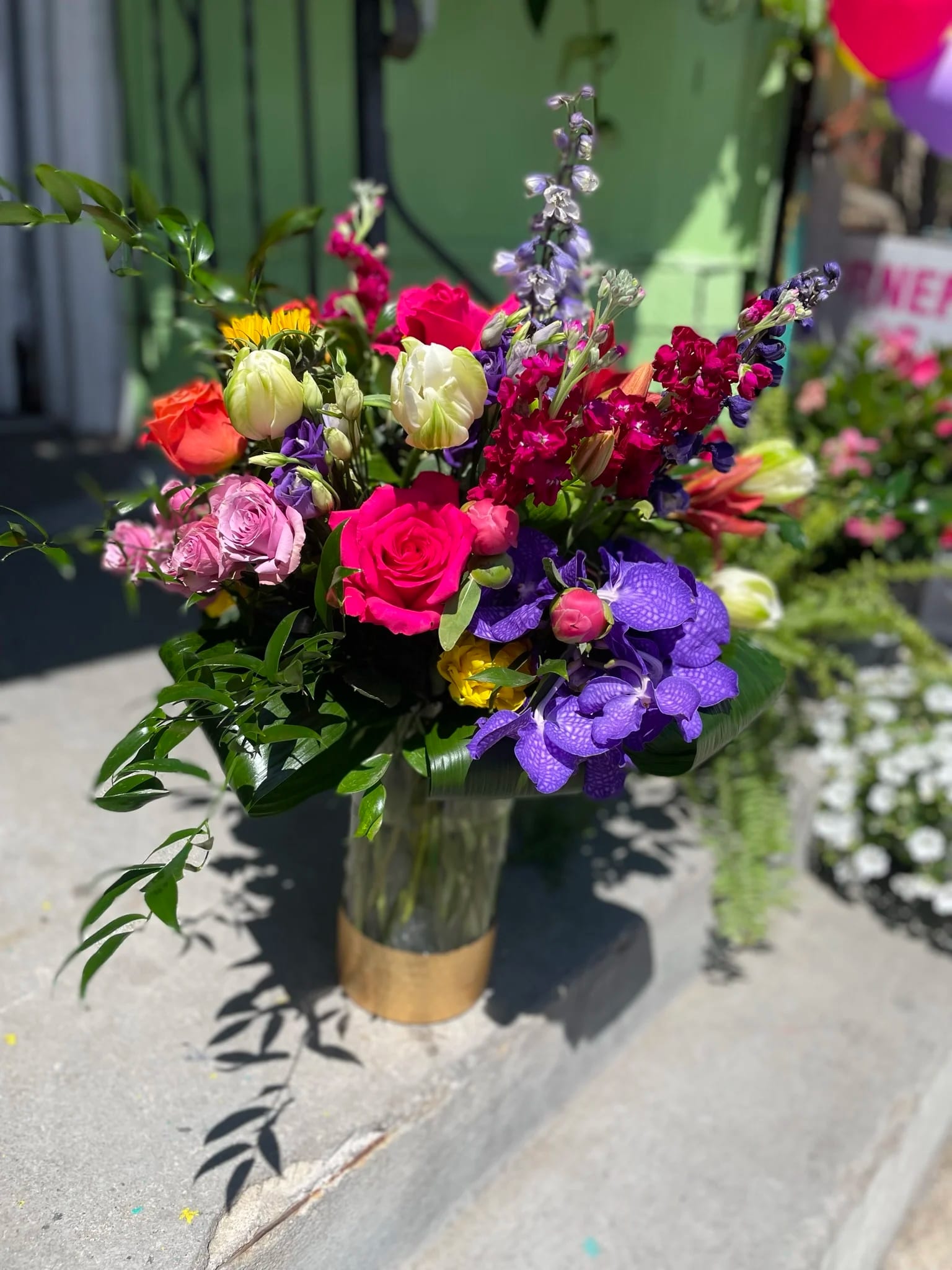 Mamba Mix - This beautiful arrangement has gorgeous colors and the combination of colors is awe-inspiring it has sunflowers, hot pink roses, purple orchid, white tulips, Lilys, delphinium, spray roses, orange roses, stock and fresh greens.