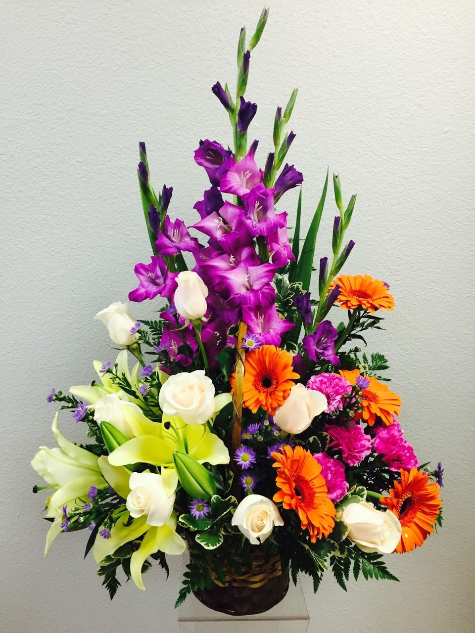 TLSP Never Forgotten - A colorful assortment of our finest blooms. Crème de la Crème roses, yellow Asiatic lilies, orange gerbera daisies, lavender gladiolus, plum carnations, and purple statice are accented with leatherleaf and sword fern stems. Gorgeously displayed in a basket, this arrangement will add to the natural beauty and serenity of their final tribute.ype a description for this product here...  