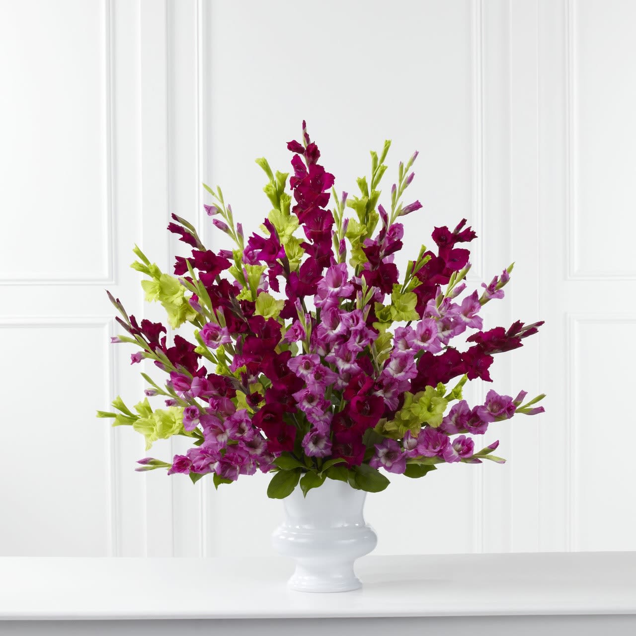 TLSP The Solemn Offering Arrangement - The Solemn Offering Arrangement is a bright and beautiful way to say your final farewell. Fuchsia, magenta and jade gladiolus are accented with lush greens and displayed in a white plastic urn to commemorate the life of the deceased wtih fantastic color and elegance. GOOD arrangement includes 25 stems. Approximately 34&quot;H x 34&quot;W. BETTER arrangement includes 31 stems. Approximately 35&quot;H x 35&quot;W. BEST arrangement includes 37 stems. Approximately 36&quot;H x 36&quot;W.  Your purchase includes a complimentary personalized gift message.