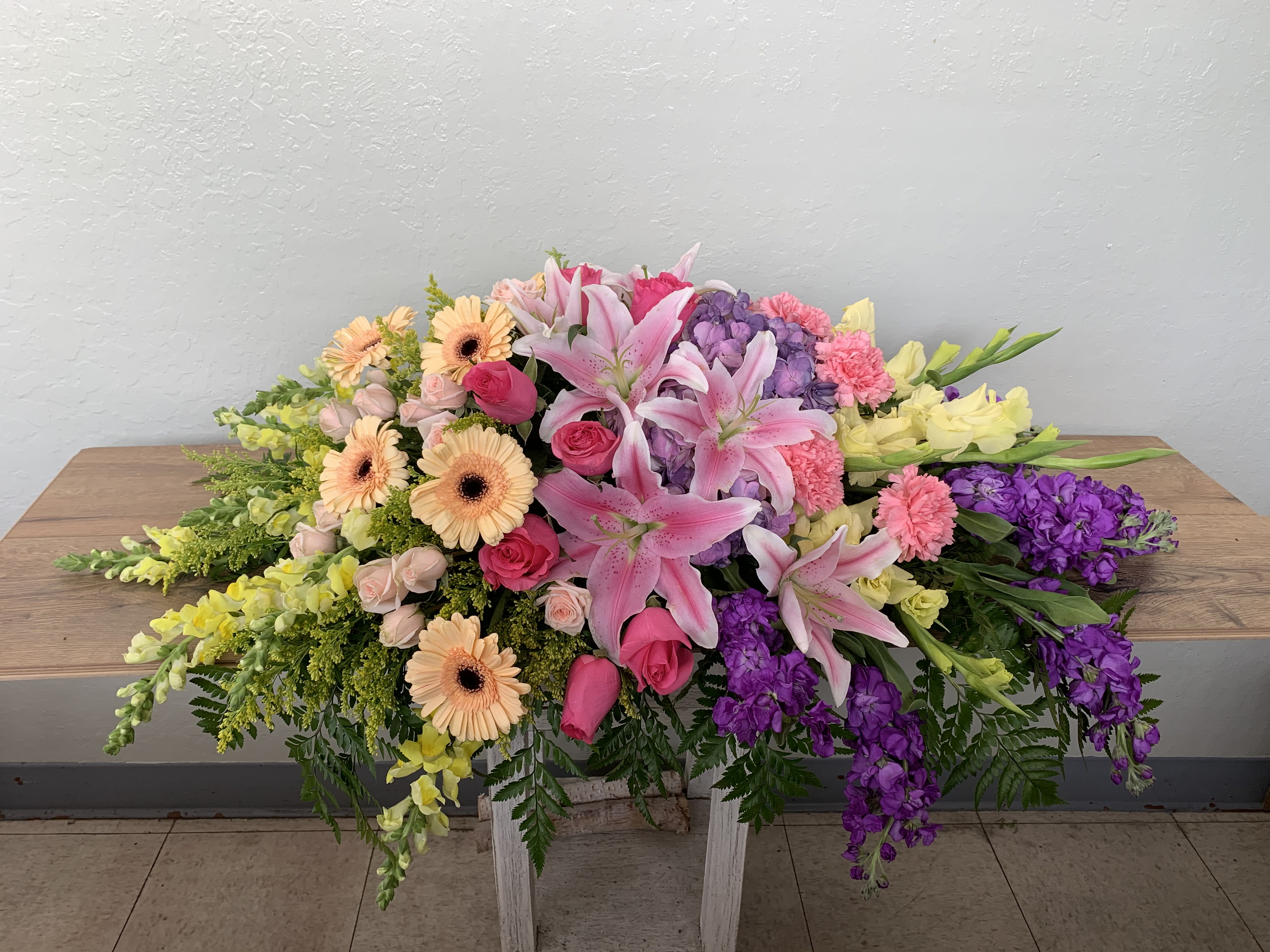 CS#17 Spring Garden Casket Spray - A garden of delicate spring colors to celebrate the life of our loved one.  The standard (half-open casket) arrangement is approximately 38” W x 16” H. The deluxe (closed casket) arrangement is approximately 46” W x 16” H