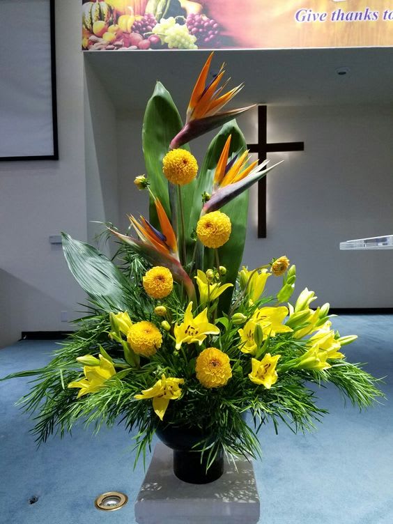 "Spiritual Sunshine" "Spiritual Sunshine" - Tropical "ARTIFICIAL" floral arrangement with bright yellow and orange flowers with a variety of greenery. This arrangement is an ideal keepsake for a memorial service or to send to the home of the family.