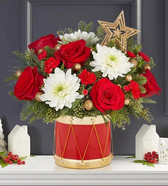 Musical Merriment - EXCLUSIVE The joy of gift-giving comes alive in our bright and festive arrangement. We’ve gathered red &amp; white blooms, Christmas greens, glittery gold ornaments and a gold star in our exclusive Musical Merriment drum container, inspired by the Nutcracker. Full of vintage charm, it’s a gift that delivers the magic of the season.