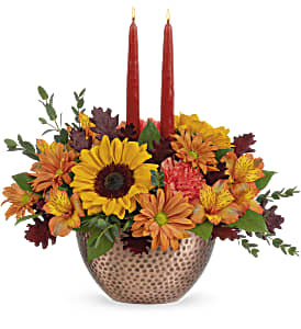 Autumn Copper Centerpiece - This stunning centerpiece features medium yellow sunflowers, orange carnations, bronze daisy spray chrysanthemums, orange alstroemeria, parvifolia eucalyptus and lemon leaf, accented with preserved oak leaves and taper candles. Delivered in Teleflora's Copper Beauty bowl. Approximately 15 3/4&quot; W x 15&quot; H With its shimmering, copper-hued bowl, radiant mix of sunflowers and glowing tapers, this stunning centerpiece celebrates the bountiful beauty of fall!