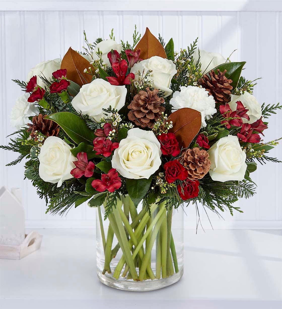Spirit of the Season Spirit of the Season - All-around arrangement with white roses and carnations; red Peruvian lilies (alstroemeria); burgundy mini carnations; accented with assorted Christmas greenery and pinecones Artistically designed in a clear glass cylinder vase Large arrangement measures approximately 14.5"H x 12.5"W Medium arrangement measures approximately 14"H x 12"W Small arrangement measures approximately 13"H x 11"W Our florists hand-design each arrangement, so colors, varieties and container may vary due to local availability To ensure lasting beauty, Peruvian lilies may arrive in bud form and will fully bloom over the next few days