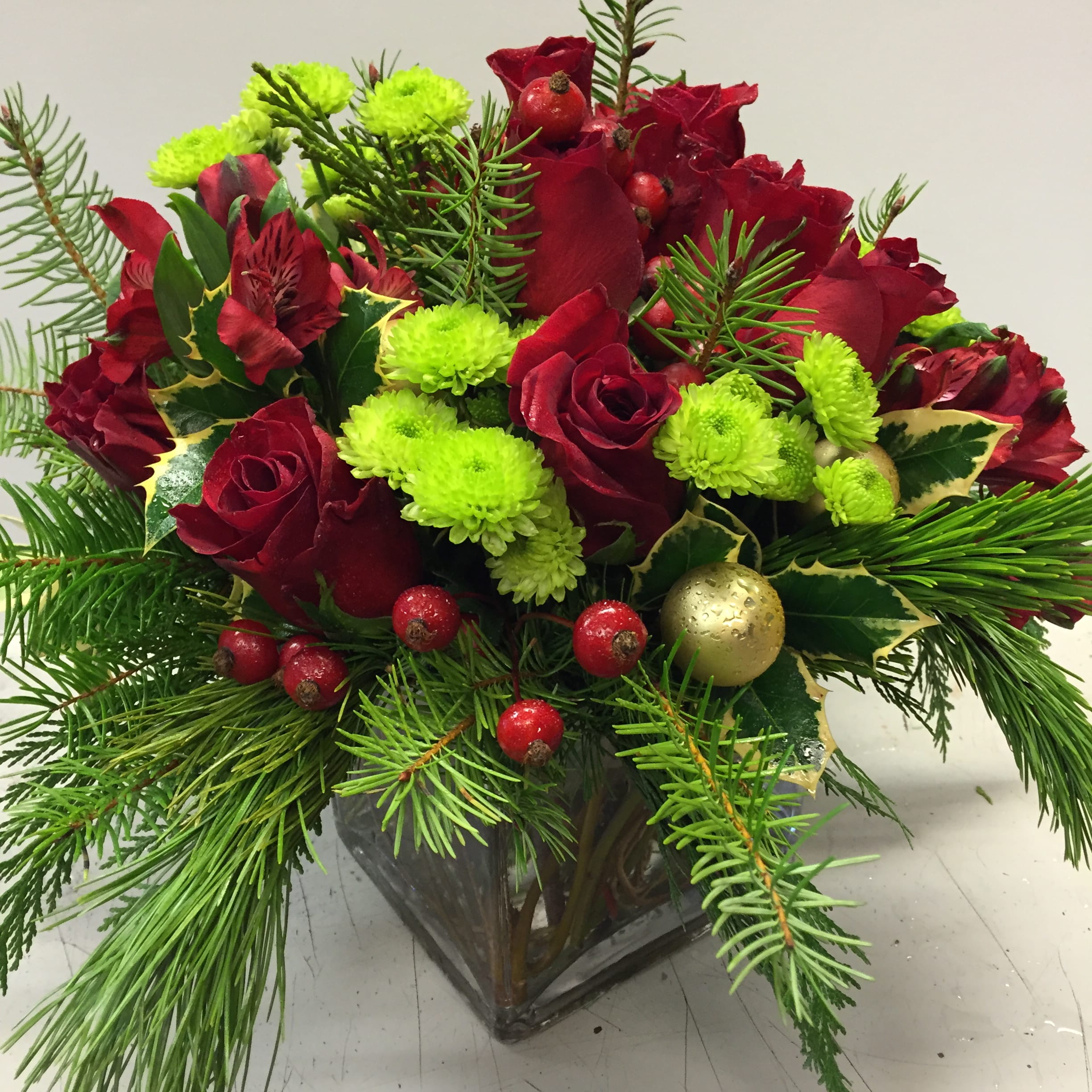 Merry &amp; Bright - A low glass vase in a Christmas theme with red roses, Christmas evergreen, mini holiday ornaments and accents.     