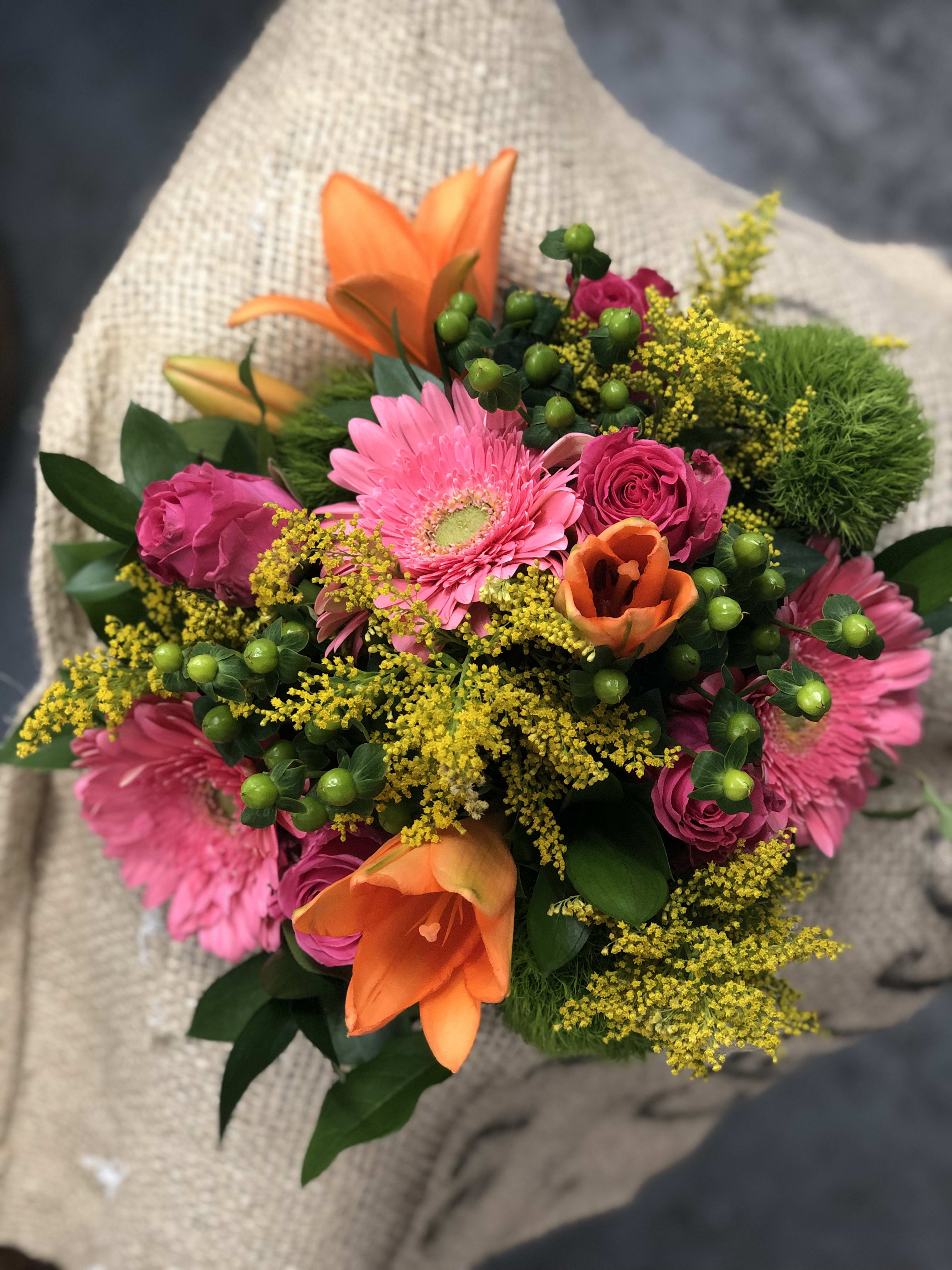 WRAP- Celebrate Today! - This beautifully designed hand wrapped bouquet is filled with happy flowers like pink roses, gerbera daisies, and bright orange asiatic lilies accented by green berries and other mixed flowers.  The wrapped bouquet comes delivered in a flower caddie with water for transport.  We call this bouquet - Vase Ready - all you need is a nice glass vase to drop the flowers in!