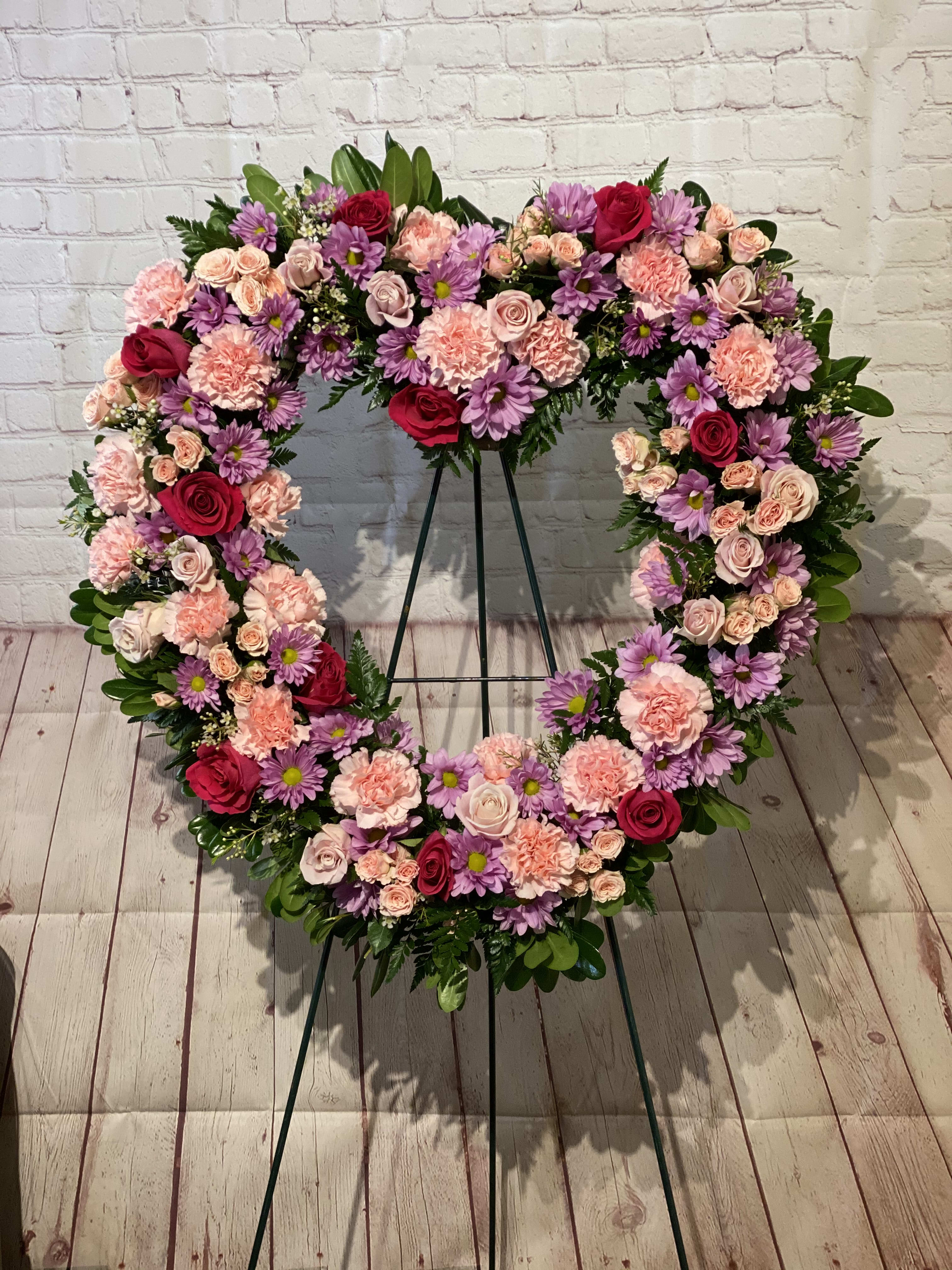 With Open Hearts With Open Hearts - Filled with roses, daisies, and more, all in shades of pink and lavender, this open heart standing spray is appropriate to send to the funeral home or service