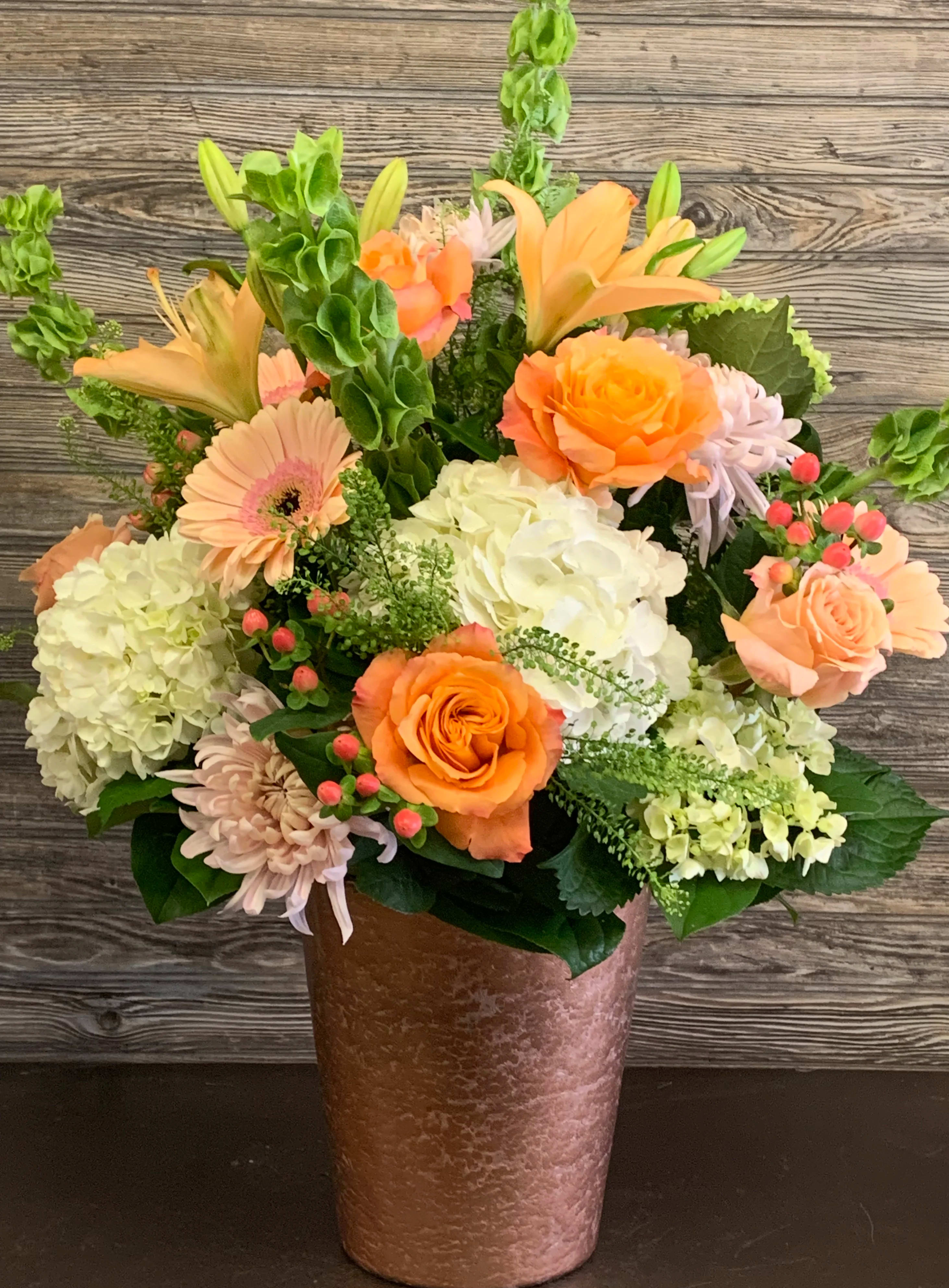Peachy Keen  - Shades of Pink, Peaches and Pistachio Greens arranged in a garden-style assortment of hydrangeas, bells of Ireland, roses, cremons, lilies, greenery, fillers, &amp; berries. Arranged in a cooper mercury vase that is 9hx7w.  The arrangement designed is about 25hx20w.   