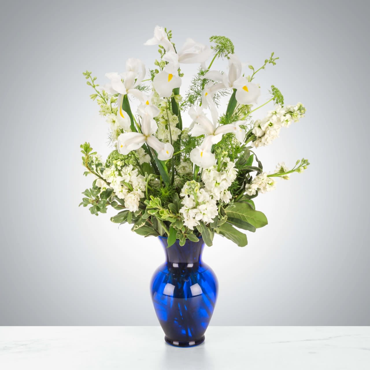 Crystal Symphony Crystal Symphony - This arrangement includes white iris, white stock, white snapdragons, and queen anne's lace in a blue vase. Send your condolences with Crystal Symphony by BloomNation™™. Approximate Dimensions: 22"D x 30"H