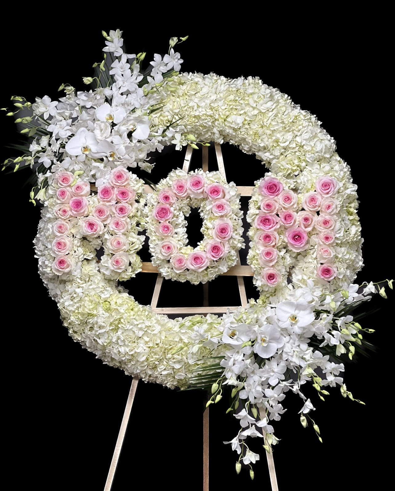 Large round spray with letters - This luxurious premium size round spray is designed as an addition to any memorial service. This arrangement highlights white hydrangeas that will ease the minds and comfort the souls that are grieving with Dendrobium and Phalaenopsis orchids and roses to represent the vibrance of their life. Colors are adjustable by request. The price includes printed ribbon or sympathy card. The diameter for this arrangement measures more than 40 inches.