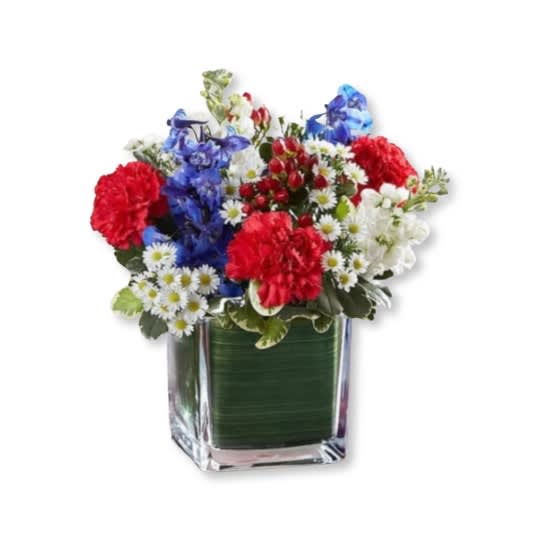 Red, White &amp; Blue Cube - It’s beautiful to honor one who held their country dear with a patriotic homage. Our arrangement of red roses, white stock, and blue delphinium, expertly gathered in a clear glass cube lined with Ti leaf ribbon, makes for a respectful and exquisite gesture. 