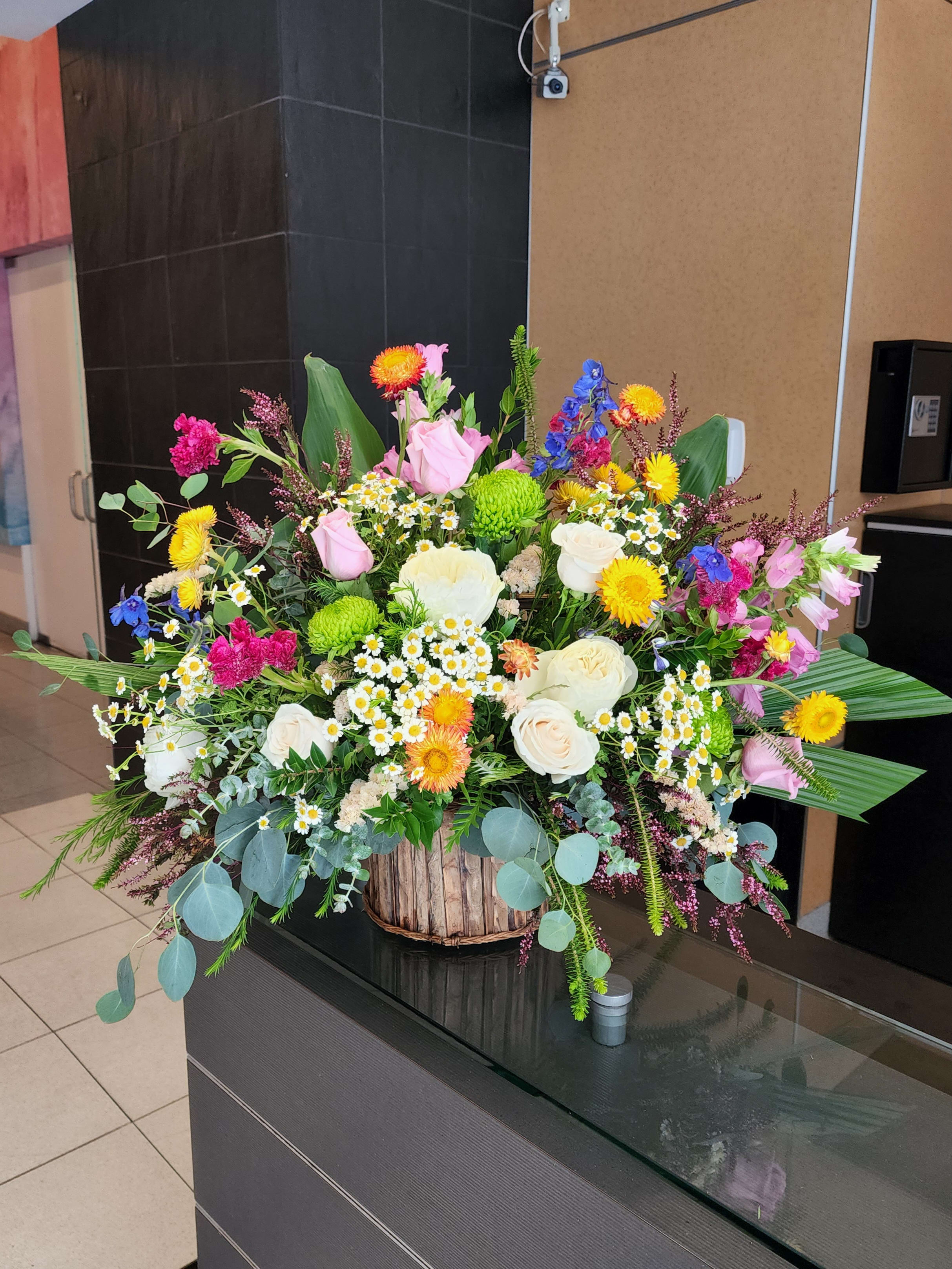 Cinnamon by Barrio Logan Florist  - Summer floral on a woodsy basket. Would look great at any lobby. Make someone day Beautiful with this floral.   