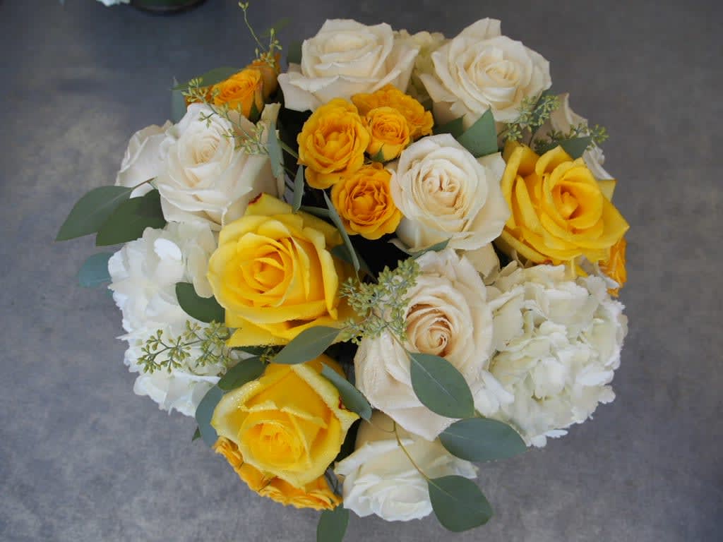 Gleams Gleams - White and yellow arrangement with touched of greens. 5" clear vase cylinder with green leaf.