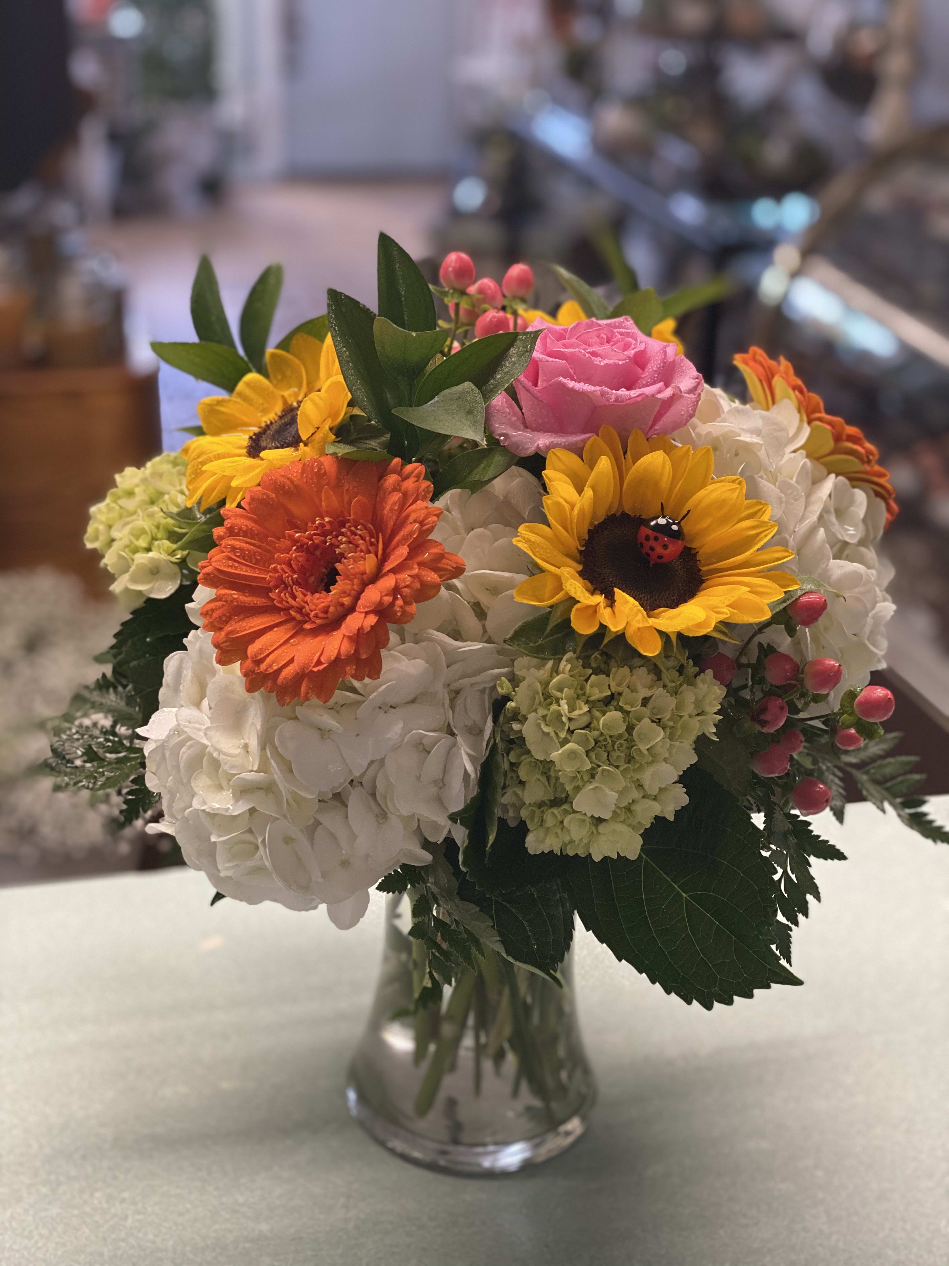Happiness In a Vase - White hydrangeas, mini green hydrangea, sunflowers (with an adorable ladybug), roses, gerber all arranged beautifully in a clear glass vase