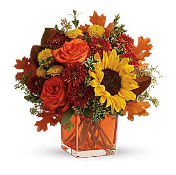 Hello Autumn Cube  - This bright bouquet includes orange roses, yellow sunflowers, gold cushion spray chrysanthemums, rust cushion spray chrysanthemums, artfully designed with several types of textured greenery and festive autumn leaves in a contemporary orange cube vase. 
