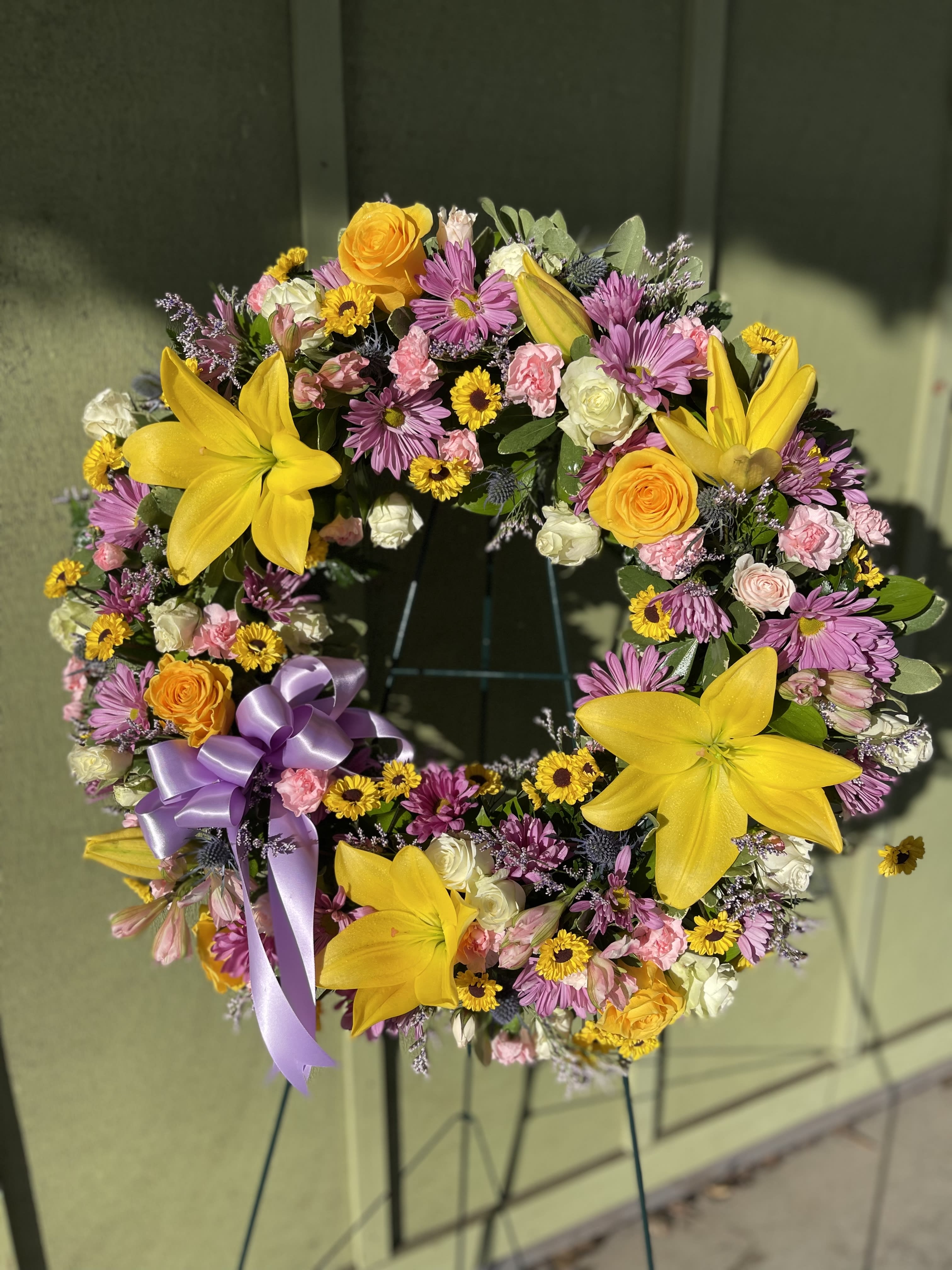 Warm Thoughts Wreath - A bright standing wreath of greenery and fresh flowers in yellow, pink, blue and white will send a message of hope and harmony, and help to celebrate a meaningful life.