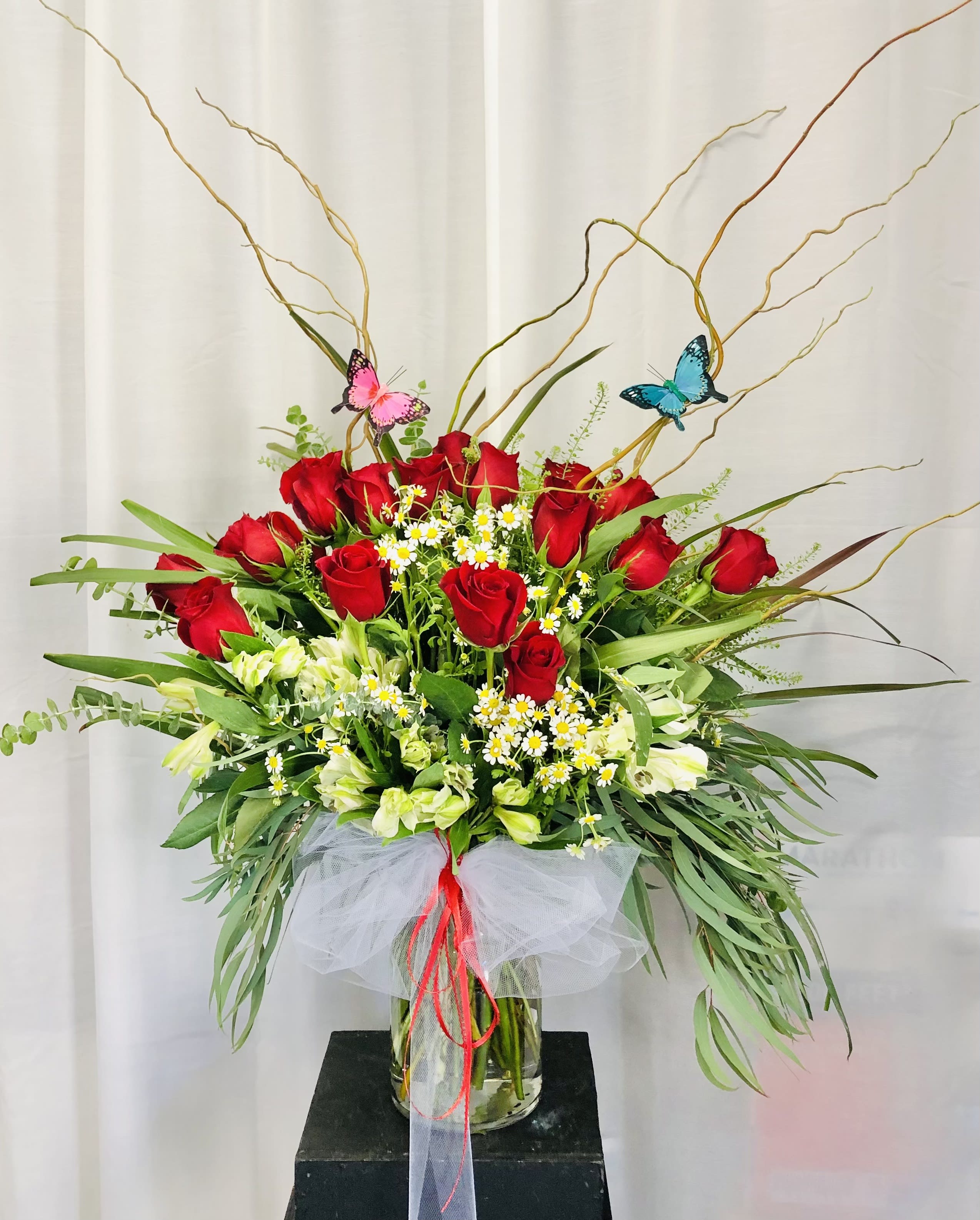 Rose Butterfly - Beautiful red and white vase arrangement featuring roses, bellium daises, green leaf accents, and thin branches.