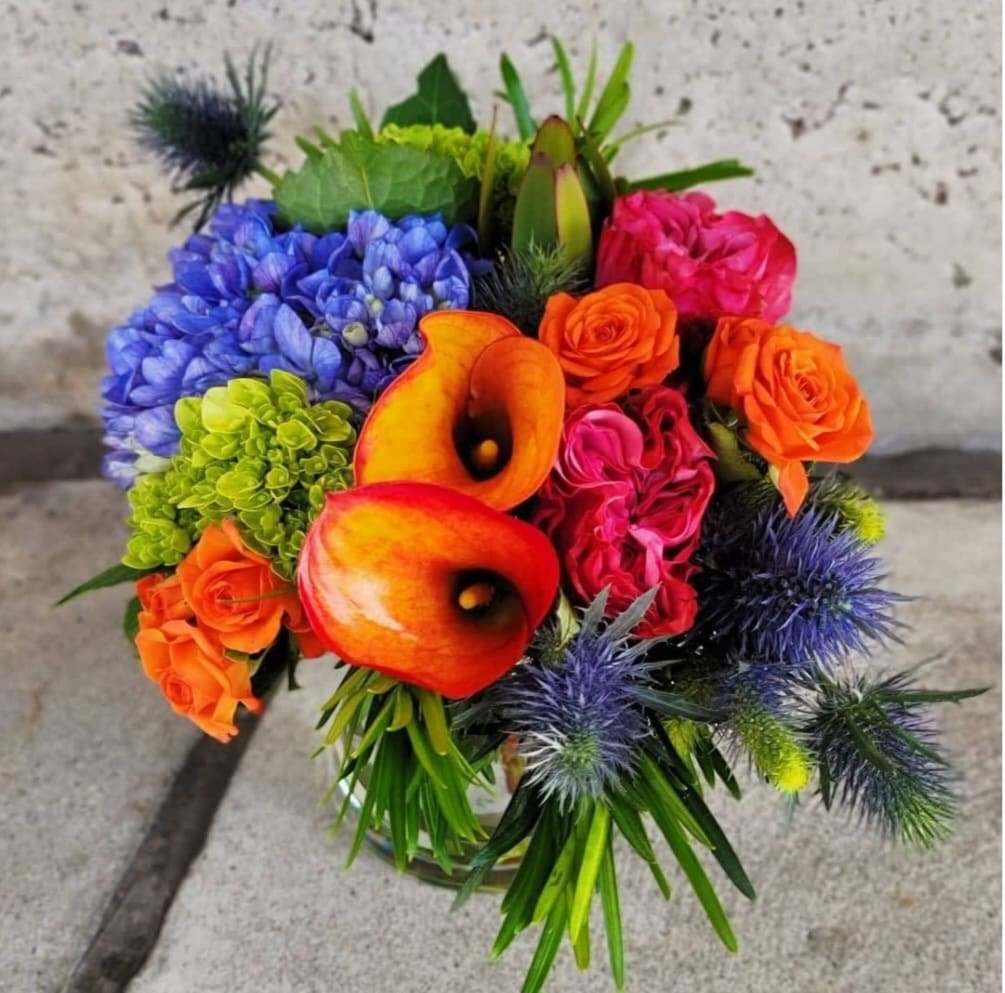 Camille Camille - A mix of nice summery flowers with a touch of a blue hyadrangea and orange callas, mojito hyadrangea and spray roses.