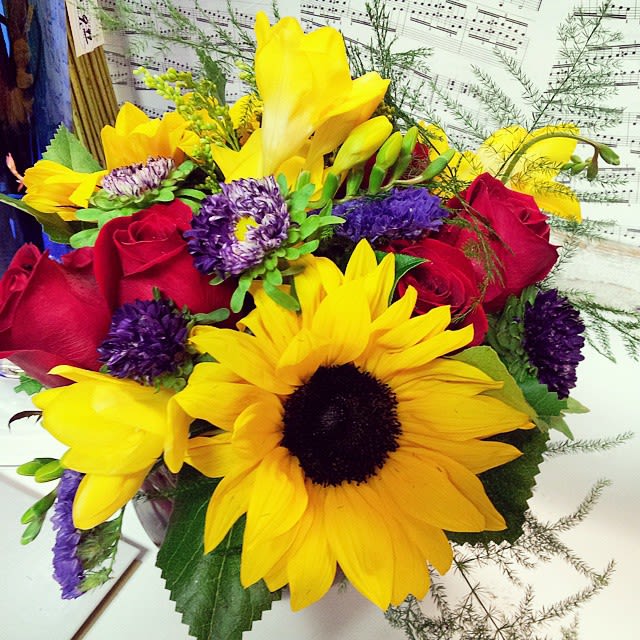 Blossoming Sunshine - This beautiful and bright bubble bowl arrangement is designed using sunflowers, red roses, freesia, solidargo, matsumoto asters, statice, and filler greens. Dimension: 12&quot;x10&quot;