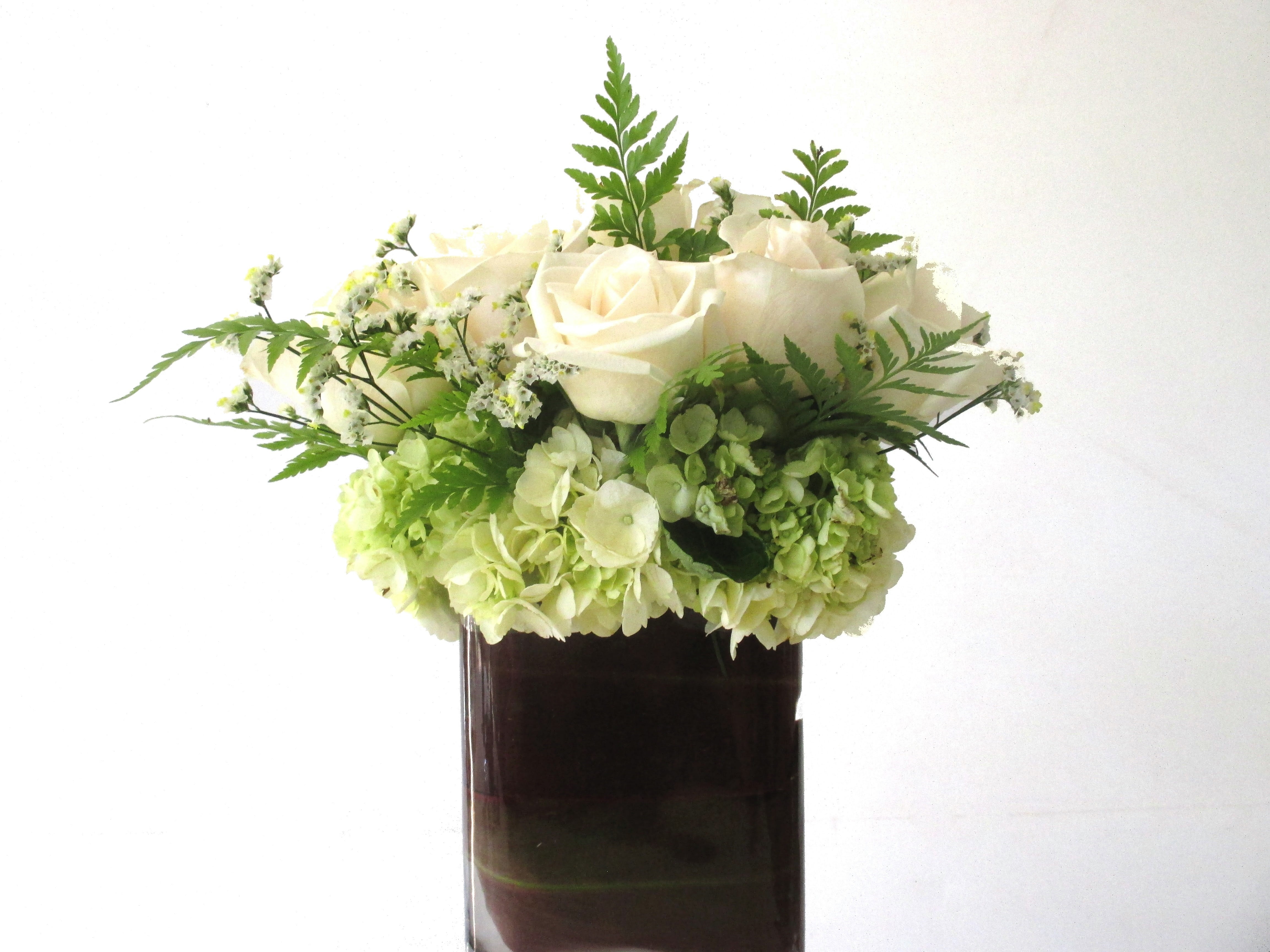 Sixer - The perfect  addition to make anyone's day.  A collection of six white roses, with hydrangea and ferns in a leaf wrapped vase.  